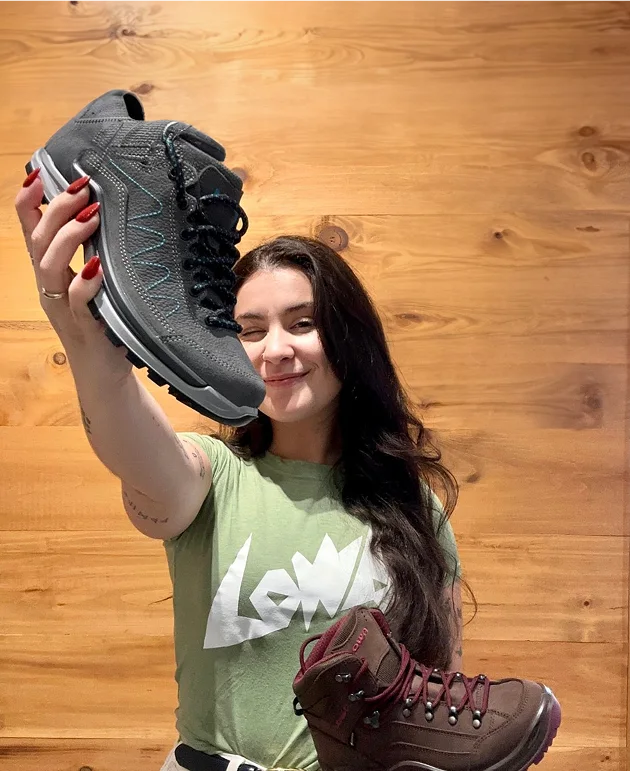 Femme souriante tenant deux chaussures de randonnée