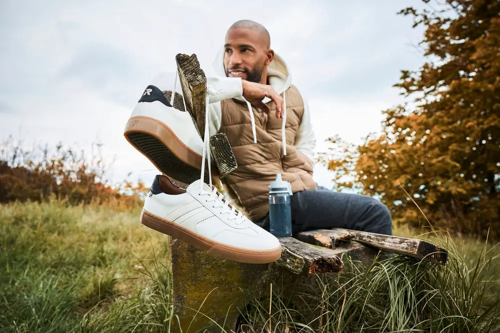 Homme assis avec chaussures suspendues, nature en arrière-plan.