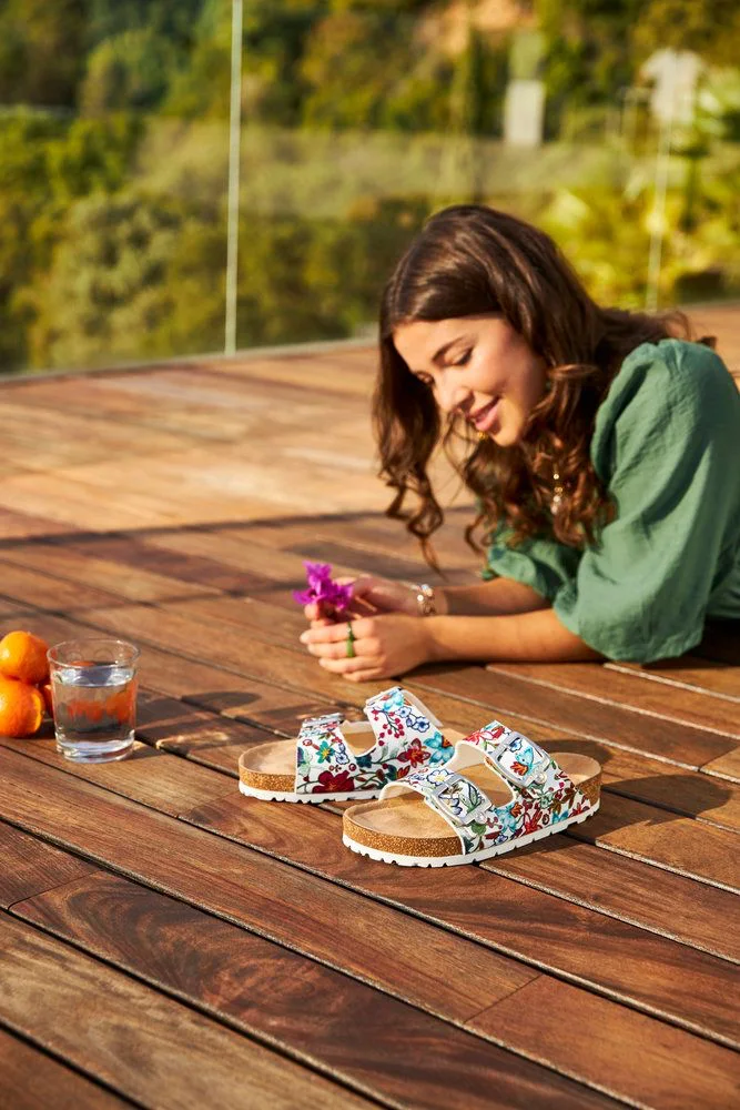 Femme allongée près de sandales fleuries sur terrasse.